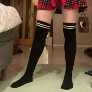 Knästrumpor  - Söta svarta knästrumpor med två vita ränder upptill. Perfekta för en sportig look eller att bära till kjol. De är långa och når upp till knäna, vilket ger en stilig och trendig känsla.