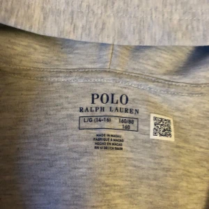 Grå hoodie från Ralph Lauren - Säljer en stilren grå hoodie från Ralph Lauren med dragkedja och klassisk logga på bröstet. Perfekt för en avslappnad look. Den har en bekväm passform och är tillverkad i mjukt material. Storlek 160!