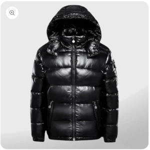 Svart pufferjacka med huva - Snygg svart pufferjacka med glansig finish och praktisk huva. Jackan har dragkedja framtill och två fickor med dragkedjor. Perfekt för kyliga dagar när du vill hålla värmen med stil.