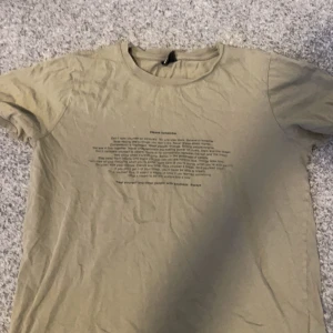 Beige t-shirt från Gina Tricot - Säljer en beige t-shirt från Gina Tricot med ett inspirerande tryck på framsidan. T-shirten har en rund halsringning och korta ärmar. Perfekt för en avslappnad stil.