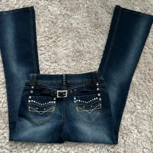 Mörkblå vintage lowrise bootcut jeans  - Snygga mörkblå lowrise bootcut jeans med dekorativa nitar på fickorna. Perfekta för en stilren look. Helt oanvända 🌟Midjemått: ca 38cm och Innerbenslängd: ca 78-79cm