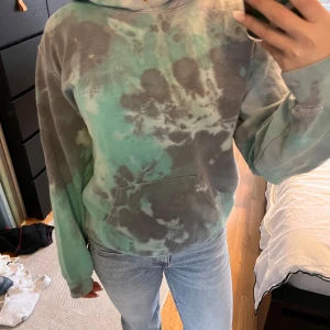 Grön och grå tie-dye hoodie från Urban Outfitters  - Säljer en cool hoodie från Urban Outfitters i grönt och grått med ett unikt batikmönster. Den har en klassisk känguruficka och en bekväm huva. Perfekt för en avslappnad stil! 💙💚