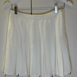 Vit plisserad kjol - Snygg vit plisserad kjol med en klassisk design. Perfekt för en stilren look. Kjolen har en kort längd och är gjord i ett lätt material som ger ett fint fall.