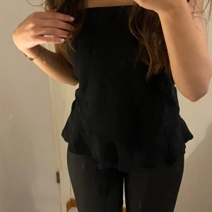 Svart topp/kjol - Snygg svart axelbandslös topp med volangdetaljer. Perfekt för en stilren look. Passar bra till jeans o kostymbyxor. Man även ha den som kjol om man vill det!🪐❤️