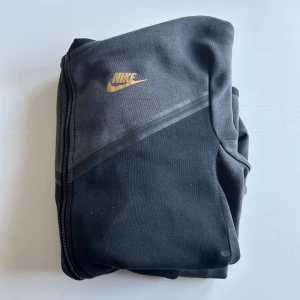 Nike tech fleece  - Säljer en Nike tech fleece. Den har en guldfärgad Nike-logga på bröstet och en praktisk ficka med dragkedja på ärmen. Priset är inte hugget i sten så hör av er vid minsta fundering!