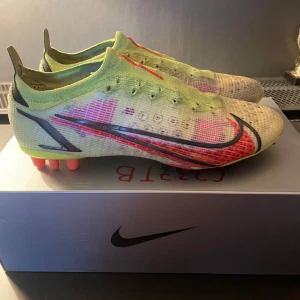 Nike Mercurial  - Snygga Nike Mercurial fotbollsskor i en fräsch kombination av gul och röd med svarta detaljer. Skorna har en strömlinjeformad design med snörning och är perfekta för snabba rörelser på planen.