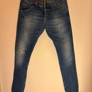 Dondup Sam Blå jeans med slitningar - Snygga blå jeans med coola slitningar och en klassisk femficksdesign. De har en normal passform och är perfekta för en avslappnad stil. Midjan är midwaist och storleken är w33. Perfekta för dig som gillar en trendig look! Toppen skick passar 175-185cm vikt spelar ingen roll.