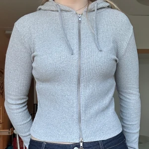 Grå zip-hoodie - Grå ribbad hoodie med dragkedja. Tröjan har tight passform, använd endast två gånger.