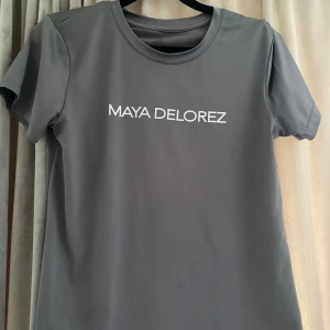 Grå t-shirt från Maya Delorez - Säljer en stilren grå t-shirt från Maya Delorez. Den har en klassisk rund hals och korta ärmar. Perfekt för en avslappnad look eller som basplagg i garderoben. Använd max fem gånger, i nyskick.