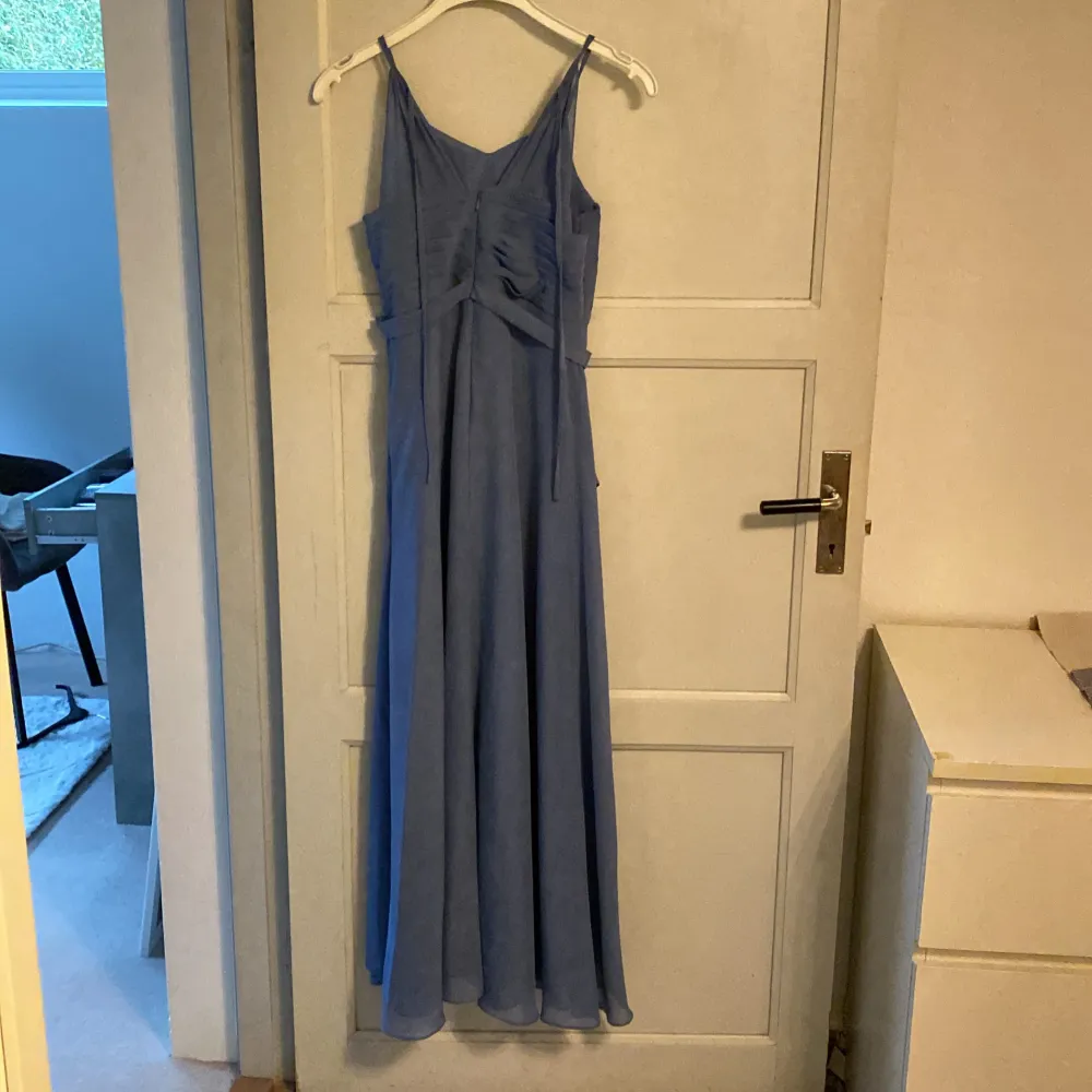 Säljer en elegant blå långklänning med smala axelband och en vacker volangdetalj på sidan. Perfekt för sommarens fester eller en bal. Klänningen har en figursmickrande passform och är tillverkad i ett lätt och luftigt material. priset kan diskuteras. Mekot.