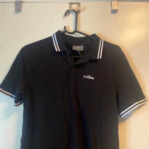 Svart piké  - Svart piké från Hm med vita detaljer. Storlek S Köpt på her avdelningen. Litet vitt tryck. Ny skick Använts 1 gång 