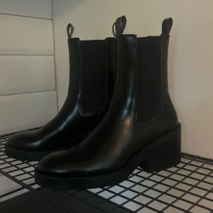 Svarta chelsea boots i skinn - Snygga svarta chelsea boots i skinn med en robust klack. De har en klassisk design med elastiska paneler på sidorna för enkel på- och avtagning. Aldrig använda pga fel storlek!❣️Nypris 799 kr.