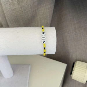 Gult och svart armband med bokstäver - Säljer ett coolt armband med gula och svarta pärlor och bokstäverna 'AIK'. Perfekt för att visa ditt stöd på matchen eller bara som en snygg accessoar till vardagsoutfiten!