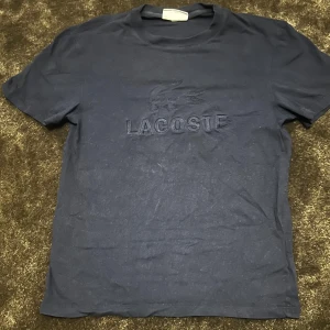Svart t-shirt från Lacoste - Säljer en snygg svart t-shirt från Lacoste. Den har en diskret logga på framsidan och lacoste loggan på baksidan nära nacken. T-shirten är i regular/slim fit och passar perfekt för en avslappnad stil. Perfekt för både vardag och fest! Skulle säga att tröjan passar för folk mellan 165-172 cm! Kom privat vid frågor eller behov av fler bilder!✌🏻💯