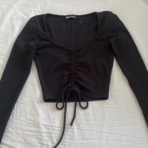 Svart ribbad topp från Zara - jag säljer en snygg svart ribbad topp från Zara. den är långärmad och har en knytning framtill som ger en fin detalj. 
