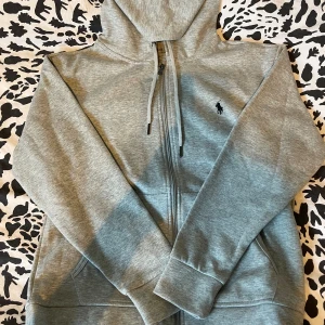 Ralph Lauren Zip Hoodie Grå - Strl S - En grå Ralph lauren zip hoodie aldrig använd. 10/10 skick säljs eftersom den aldrig kommit till användning och är i behov av lite pengar. Pris kan diskuteras :) Mvh 