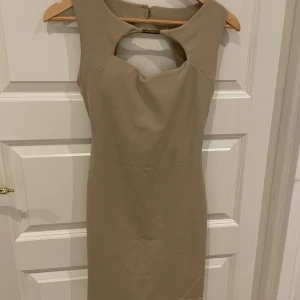 Beige ärmlös klänning med öppen rygg - Säljer en elegant beige klänning som är ärmlös och har en snygg öppen ryggdetalj. Perfekt för festliga tillfällen! Klänningen har en tight passform och är gjord i ett mjukt material som känns skönt mot huden.