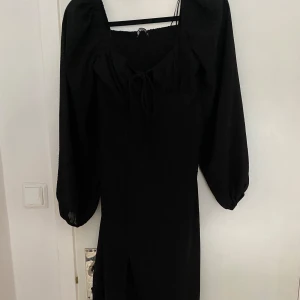 Svart långklänning med knytning - Säljer en elegant svart långklänning med långa ärmar och en fin knytning framtill. Klänningen har en smickrande passform och en subtil slits som ger en extra touch. Perfekt för festliga tillfällen! Storlek 32, PRIS KAN DISKUTERAS. 