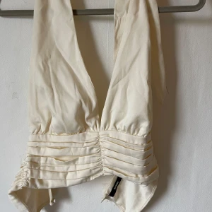 Vit halterneck topp från Bik Bok - Säljer en snygg vit halterneck topp från Bik Bok i storlek S. Toppen har en smickrande draperad design med knytning i nacken och en tight passform. Perfekt för sommarens fester eller en utekväll. 🕺✨