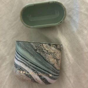 AirPods-fodral från Ideal of Sweden - Snyggt AirPods-fodral från Ideal of Sweden med ett marmorerat mönster i gröna och beige toner. Perfekt för att ge dina AirPods ett stilrent och unikt utseende. Fodralet är i mycket bra skick och skyddar dina hörlurar mot repor och stötar.