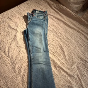 Blå bootcut jeans från True Religion - Säljer ett par snygga blå bootcut jeans från True Religion i modellen Becca. De har en midwaist passform och har coola röda och vita sömmar på bakfickorna. Super sköna och snygga! Kommer tyvärr inte till användning då de inte är min stil längre. Perfekta för både vardag och fest! 🕺