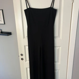 Svart långklänning med smala axelband - Säljer en elegant svart långklänning med smala axelband. Perfekt för festliga tillfällen eller en stilren kvällslook. Klänningen har en enkel och tidlös design som passar alla säsonger. Materialet känns mjukt och bekvämt mot huden.