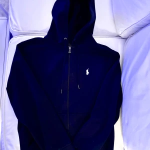 Mörkblå hoodie från Ralph Lauren XS herr - Säljer en snygg mörkblå hoodie från Ralph Lauren med dragkedja och den klassiska loggan på bröstet. Perfekt för kyliga dagar och passar till allt. Den är i mycket bra skick och superbekväm att ha på sig. Perfekt för både vardag och chill! Nypris 2295:-. Killen på bilden är 190cm lång (för liten tröja alltså😁).