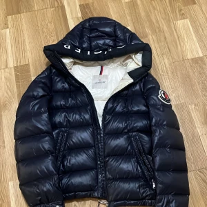 MörkBlå Jacka från Moncler - Säljer en snygg Mörkblå dunjacka från Moncler i mycket bra skick. Jackan har en stor huva med Moncler-logga och dragkedja framtill. Perfekt för kalla vinterdagar! 🖤 Säljer för 3000kr men kan ta ner priset vid snabb köp! Fraktas inte.