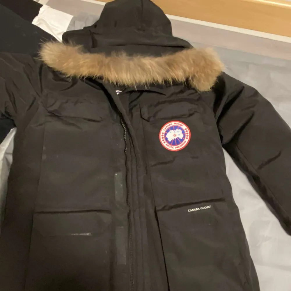 Säljer en svart Canada Goose dunjacka i mycket bra skick. Jackan har en pälsfodrad huva och är perfekt för kalla vinterdagar. Den har en dragkedja framtill och är långärmad. Märkets logga syns tydligt på bröstet. Perfekt för dig som vill hålla värmen med stil!. Jackor.