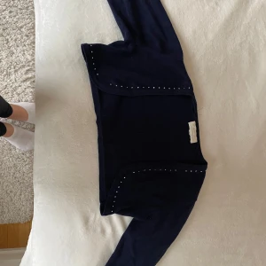 Mörkblå bolerotopp med stenar  - Säljer en elegant mörkblå bolerotopp med stebdetaljer längs kanterna. Perfekt för att piffa upp en outfit till fest eller en speciell kväll. Toppen har långa ärmar och är i mycket bra skick. Passar perfekt till både klänning och toppar.