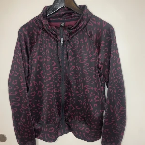 Svart och lila leopardmönstrad jacka - Säljer en cool svart och lila leopardmönstrad jacka med dragkedja. Perfekt för höst och vår, den har långa ärmar och en bekväm passform. Jackan är i mycket bra skick och passar perfekt för en avslappnad stil.