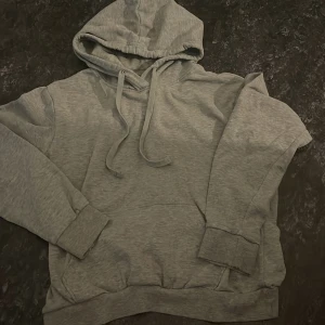 Grå hoodie - Säljer en grå hoodie i mycket bra skick. Den är perfekt för kyliga dagar med sin mjuka och bekväma passform. Hoodien har en klassisk design med dragsko i huvan och en stor ficka framtill. Perfekt för både vardag och mysiga hemmakvällar.
