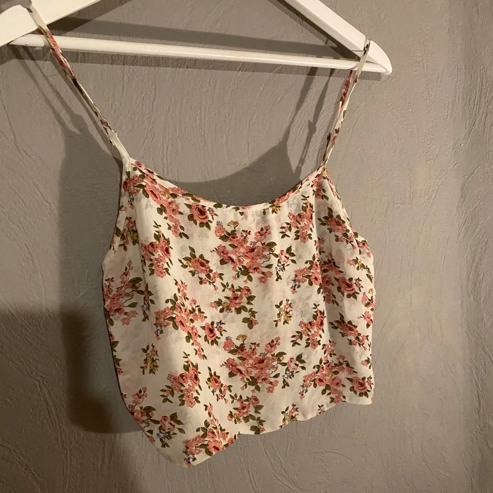 Säljer ett tunt superfint blommigt linne. Perfekt för sommardagar med sitt lätta och luftiga material. Linnet har smala axelband och ett härligt blommönster i rosa och grönt på en vit bakgrund. Passar perfekt till jeans eller shorts för en avslappnad look. (PM OM DU VILL HA FLER BILDER). Toppar.