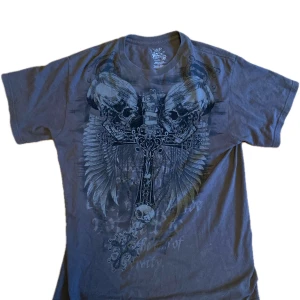 Tvär fet chemistry t shirt med vingar på ryggen - Säljer en grå brun t-shirt från Chemistry i storlek L. Den har ett coolt tryck med dödskallar och kors med vingar både fram och bak. Har dock en pytte liten fläck som man inte tänker på