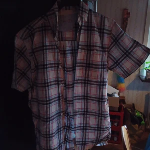 Rutig kortärmad skjorta från Dressmann stl L (40/42) - Säljer en snygg rutig skjorta från Dressmann i storlek L. Skjortan har ett klassiskt rutmönster i blått, rött och vitt. Den är kortärmad och perfekt för sommardagar. Materialet känns bekvämt och lätt, vilket gör den idealisk för både vardag och fest. Knapparna framtill ger en stilren look. Passar perfekt till jeans eller shorts!