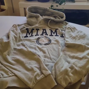 Ljus grön hoodie från 157 - Säljer en snygg ljus grön hoodie från 157 i storlek XS. Den har en cool 'MIAMI 1999' print på framsidan och en klassisk känguruficka. Perfekt för en avslappnad stil och mysiga dagar. Huvan har justerbara snören för extra komfort. Passar perfekt till höst och Vintern!