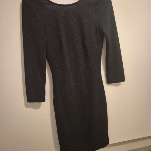 Svart glittrig klänning från Jacqueline de Yong - Snygg svart klänning från Jacqueline de Yong i storlek XS. Den har ett glittrigt mönster som gör den perfekt för festliga tillfällen. Klänningen är i ett mycket bra skick och har trekvartsärmar. Perfekt för höst och vinterfester