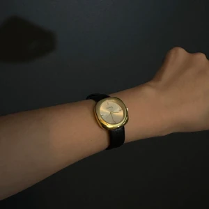 Elegant klocka med svart läderarmband - Säljer en stilren klocka med en elegant guldfärgad urtavla och svart läderarmband. Perfekt för både vardag och fest. Klockan har en klassisk design med en kvadratisk urtavla och en diskret logotyp. Passar alla tillfällen!