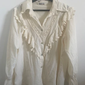 Vit blus med spetsdetaljer - Säljer en superfin vit blus med spetsdetaljer och volanger. Den har långa ärmar och knappar framtill. Perfekt för en romantisk look eller en speciell tillställning. Tillverkad i Italien, vilket ger den en extra touch av lyx. Oklart vilken storlek men passar M/L bra skulle jag säga💗💗💗💗