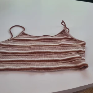 Randig ribbad topp från Shein - Säljer en superfin randig topp från Shein i bruna och vita nyanser. Den är ribbad och har smala axelband, perfekt för sommardagar. Toppen är i bra skick och passar perfekt till ett par jeans eller shorts. Perfekt för en avslappnad stil!