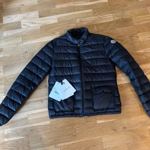 Svart dunjacka från Moncler - Säljer en snygg svart dunjacka från Moncler i mycket bra skick. Perfekt för höst och vinter, håller dig varm och trendig. Storlek S. Passar både till vardags och festliga tillfällen. Nypris ca 10000 kr men säljer för 5000