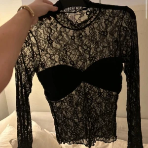 Svart spetsblus från Nelly - Säljer en elegant svart spetsblus från Nelly. Den är genomskinlig med ett vackert blommönster och har långa ärmar. Perfekt för en festlig kväll eller en utekväll med vänner. Blusen är i mycket bra skick och ger en stilren look.