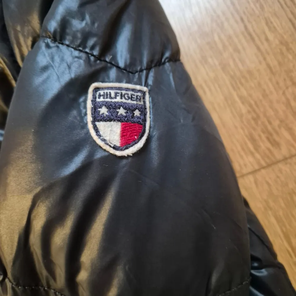 Säljer en snygg svart pufferjacka från Hilfiger Denim i bra skick. Jackan har en glansig yta med knappar och dragkedja framtill. Perfekt för kyliga dagar och ger en cool look. Passar både till vardags och lite finare tillfällen. 🖤. Takit.