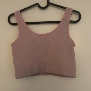 Rosa ribbad croppad topp - Säljer en superfin ljusrosa ribbad linnetopp. Den är ärmlös och croppad, perfekt för sommardagar eller som ett lager under en jacka eller träning . Toppen har en tight passform och är gjord i ett mjukt och stretchigt material.