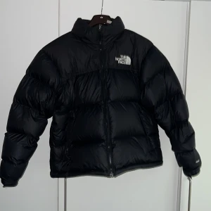 Svart dunjacka från The North Face - Säljer en svart nuptse från The North Face i storlek M. Jackan är perfekt för vintern  med sitt tjocka och varma dunfoder. Loggan syns tydligt på bröstet och ryggen. Jackan är i nyskick och oanvänd då jag köpte den i fel storlek för mig själv.