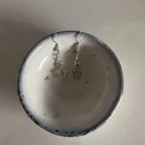 Silverfärgade stjärnörhängen - Säljer ett par superfina silverfärgade örhängen med stjärnformade hängen. Perfekta för att ge en glittrig touch till vilken outfit som helst. De är lätta och bekväma att bära hela dagen. Passar både till vardags och fest!