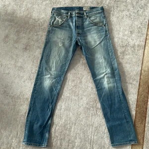 Blå jeans från Wrangler - Säljer ett par klassiska blå jeans från Wrangler. De har en snygg slitning och en straight passform. Jeansen har knappar i gylfen och är i ett robust denim-material. Perfekta för en avslappnad stil!