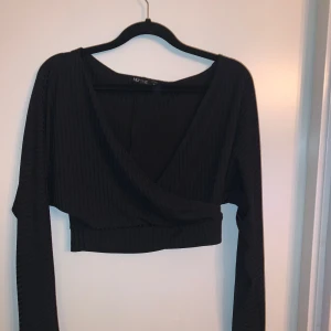 Svart omlottopp från NLY One - Säljer en snygg svart omlottopp från NLY One. Den är croppad och har långa ärmar.