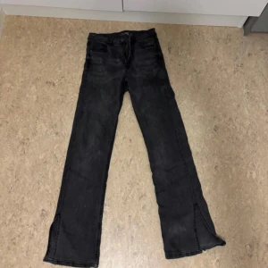 Svarta jeans med slits - Säljer ett par svarta jeans med coola slitsar vid bensluten. De har en klassisk femficksdesign och ser ut att vara i bra skick. Perfekta för en avslappnad stil eller en utekväll!