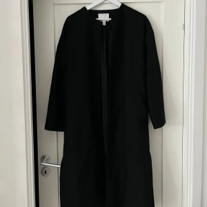 Svart kappa - Supersnygg och användbar kappa från H&M. Köpt förra säsongen. Lång i modellen, men två fickor, knytning i midjan.